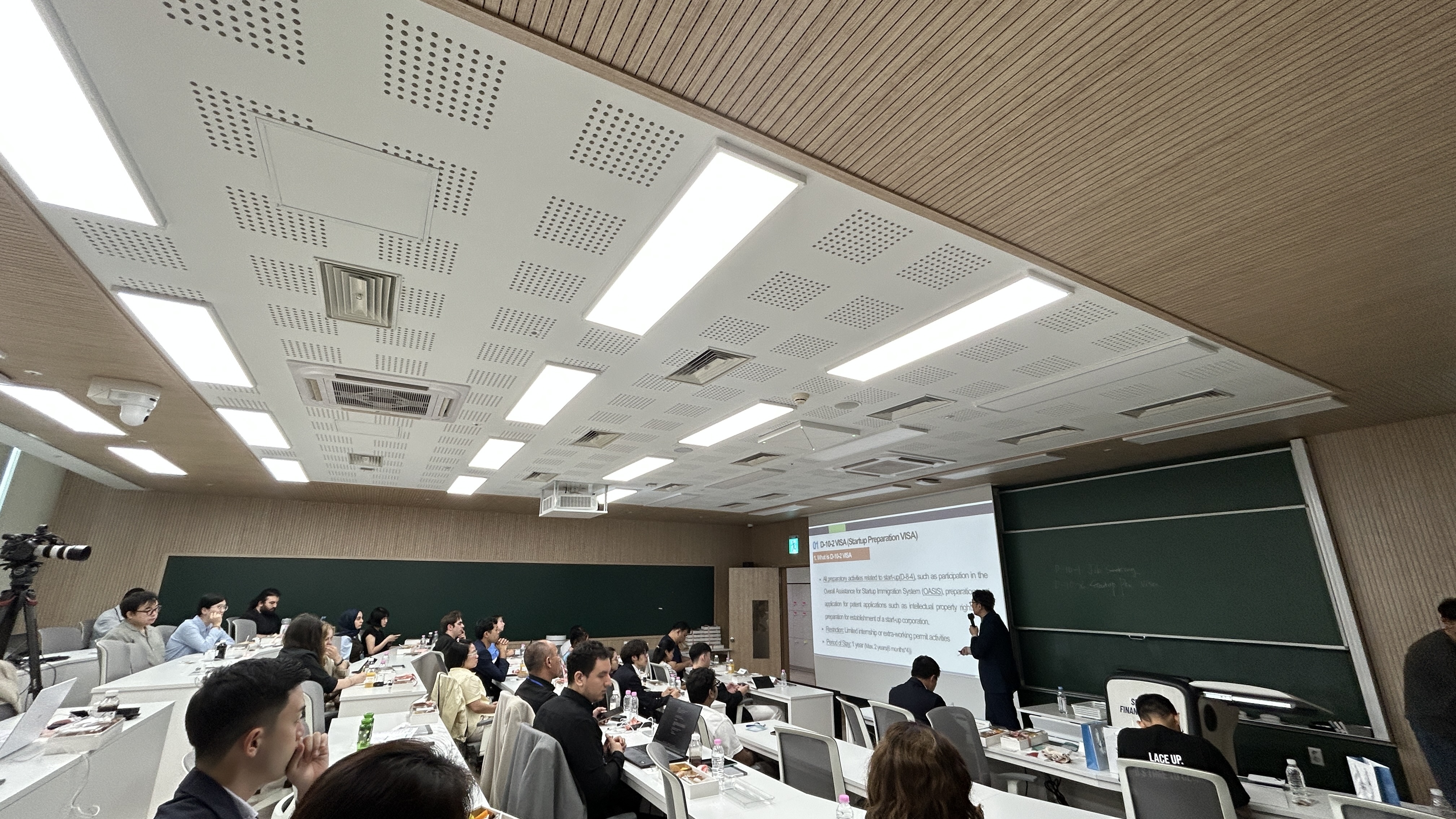 View of a room full of people listening to the presentation of the speaker.