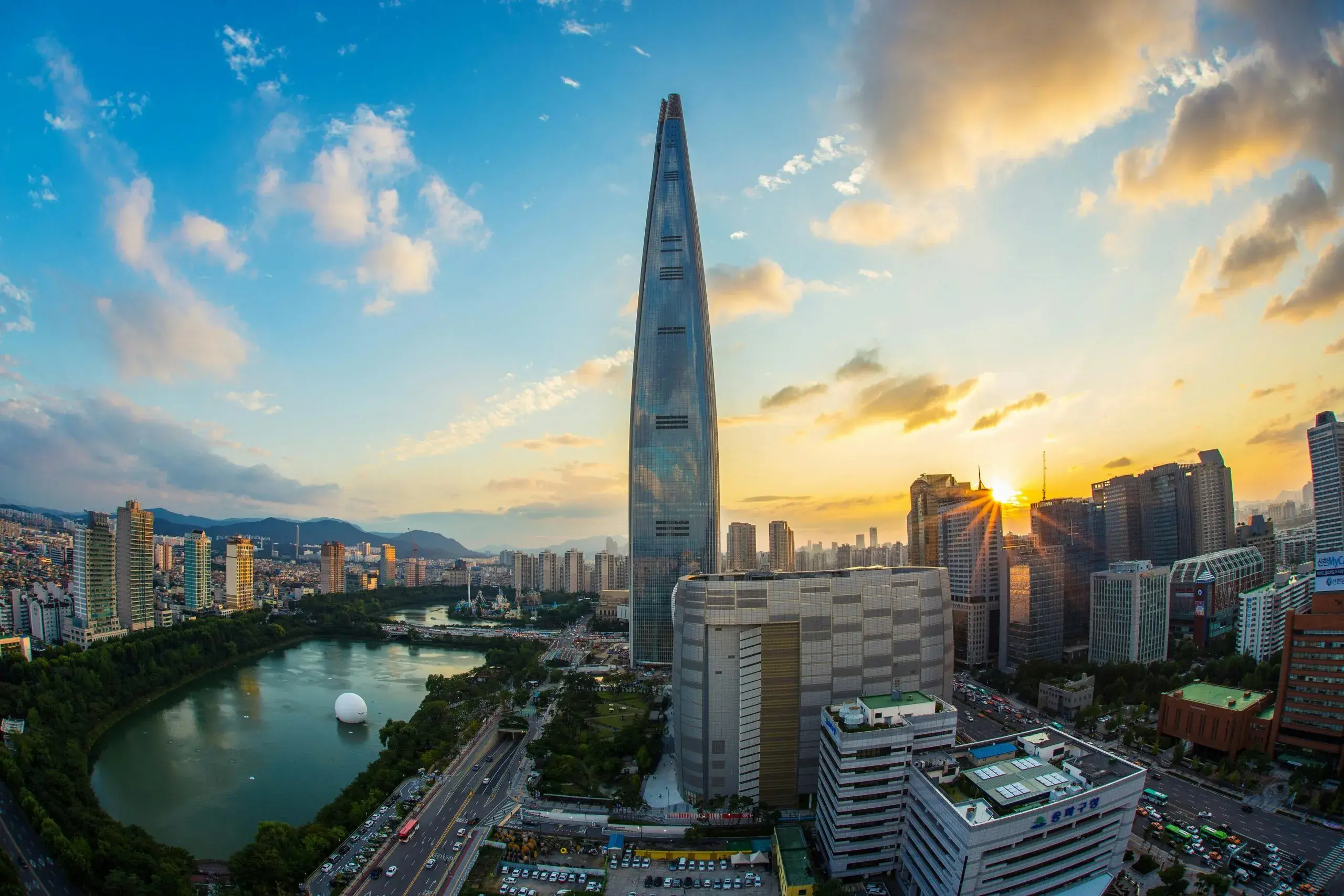 Seoul skyline at sunset featuring Lotte World Tower, city buildings, and a nearby lake.