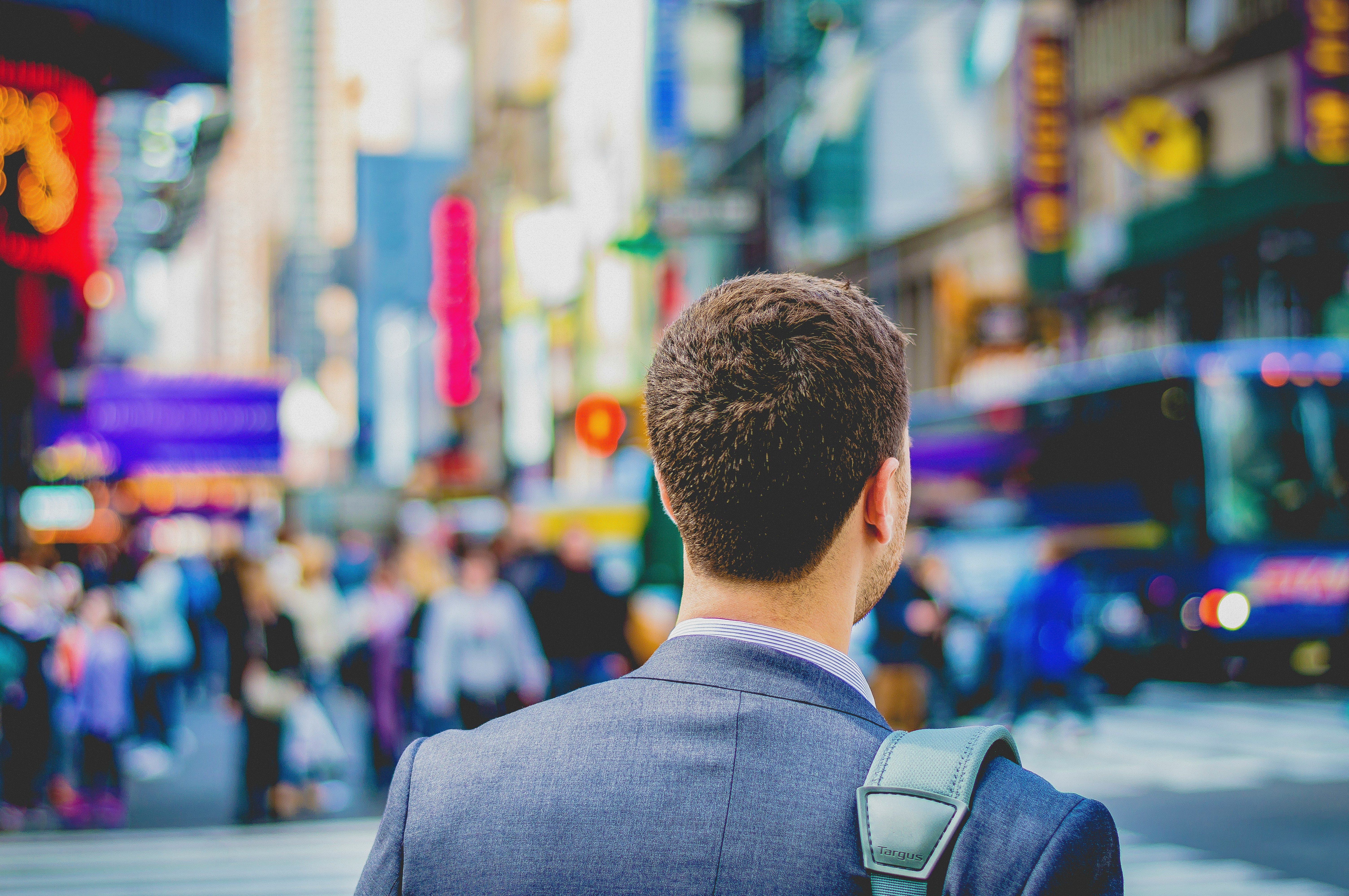 The back of a man going into the city with a bag strapped to his shoulder. 